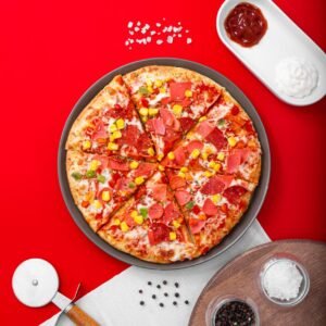 Top view of a tasty pepperoni pizza with condiments on a bold red background, perfect for food enthusiasts.