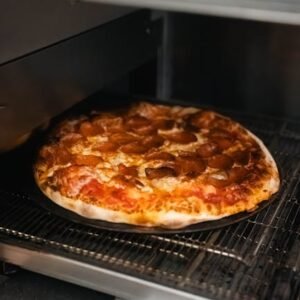 A close-up of a pepperoni pizza baking inside a commercial pizza oven.